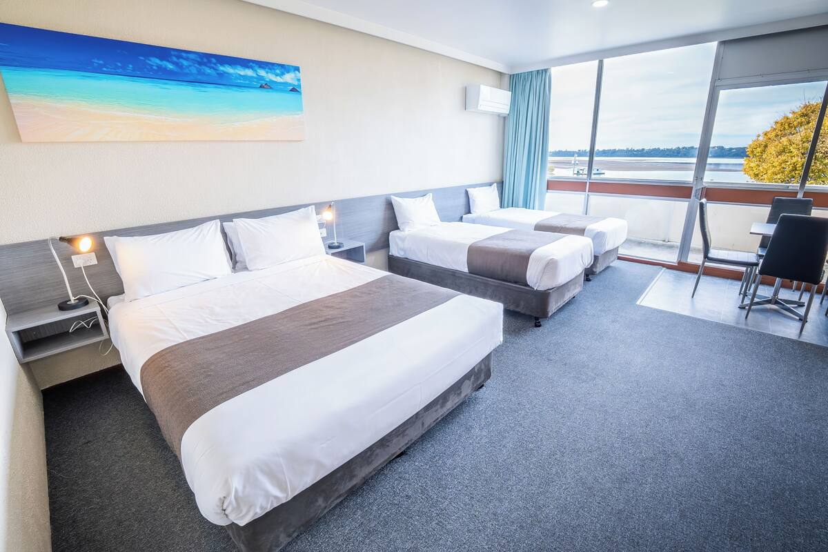 A hotel room with two beds, a balcony with a view of the water, and a painting on the wall.