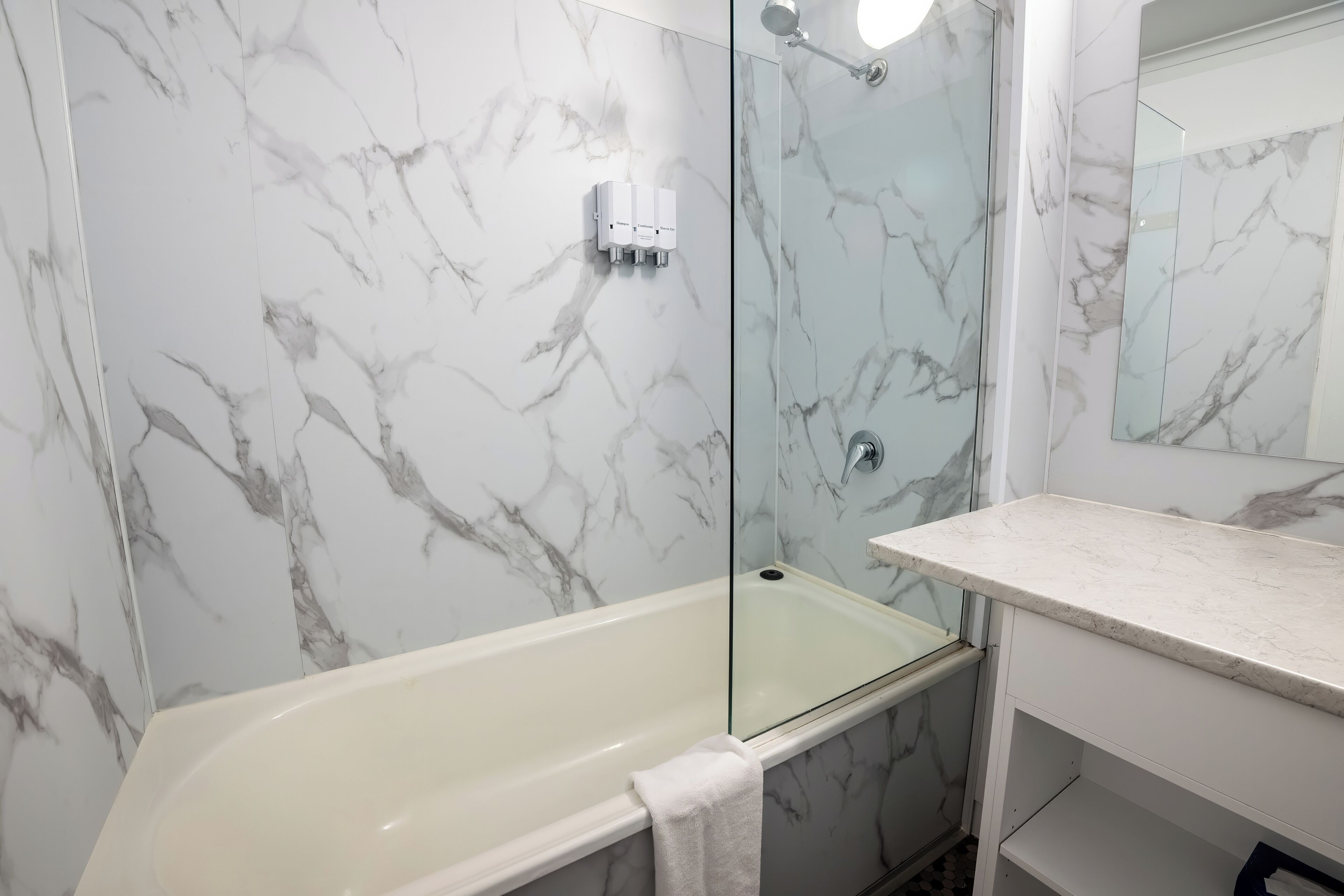 Un baño con pared de mármol, bañera, cabina de ducha de vidrio y encimera blanca.