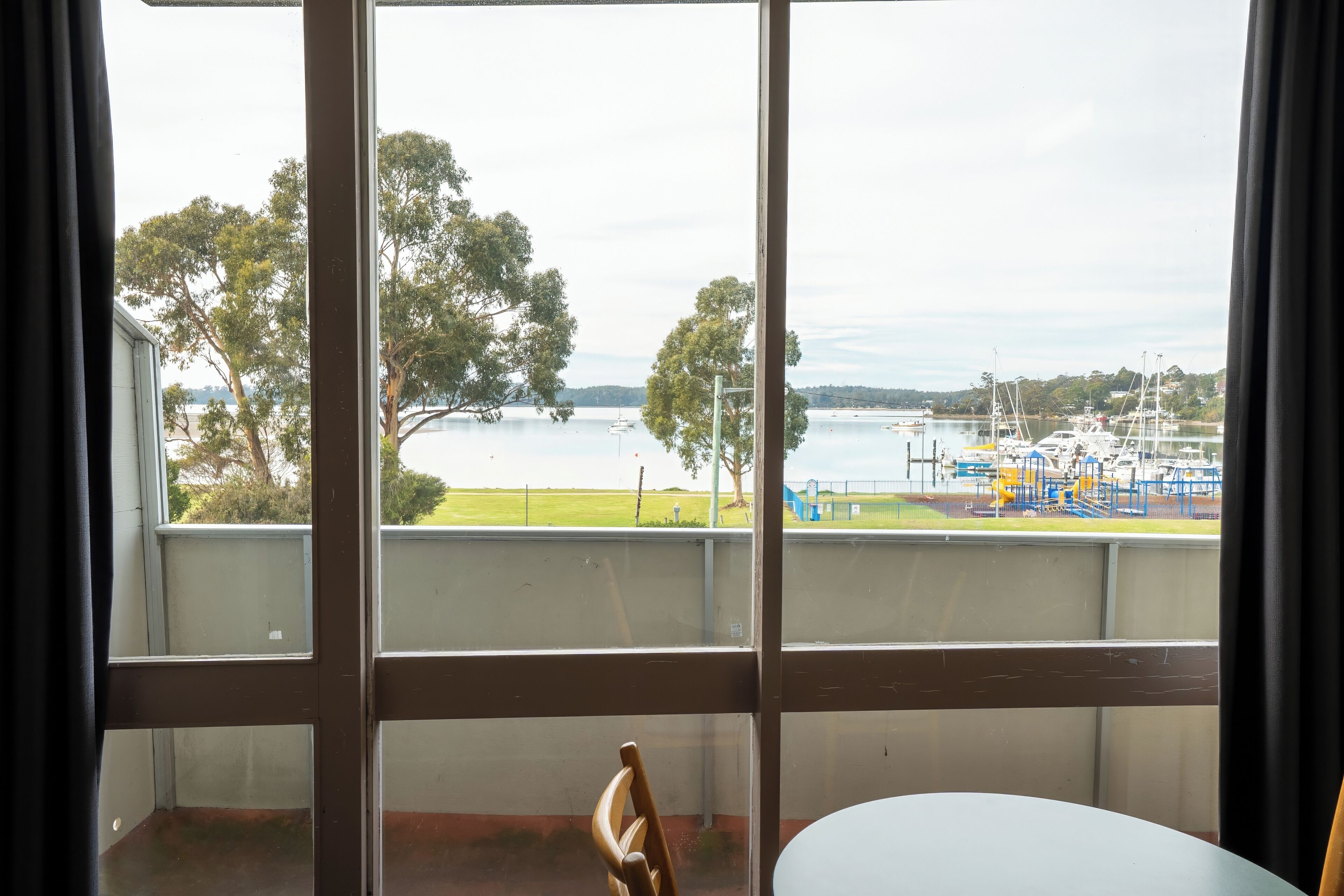 A room with a large window overlooking a marina with boats and trees.