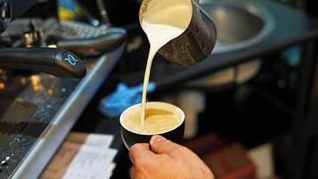 Una mano vertiendo leche en una taza de café.