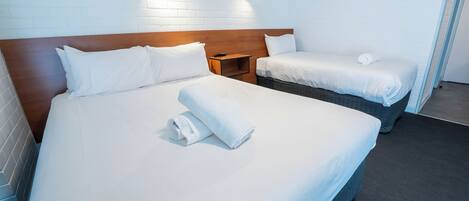 Habitación de hotel con dos camas, sábanas blancas, cabecero de madera, una mesita de noche y un cuadro en la pared.