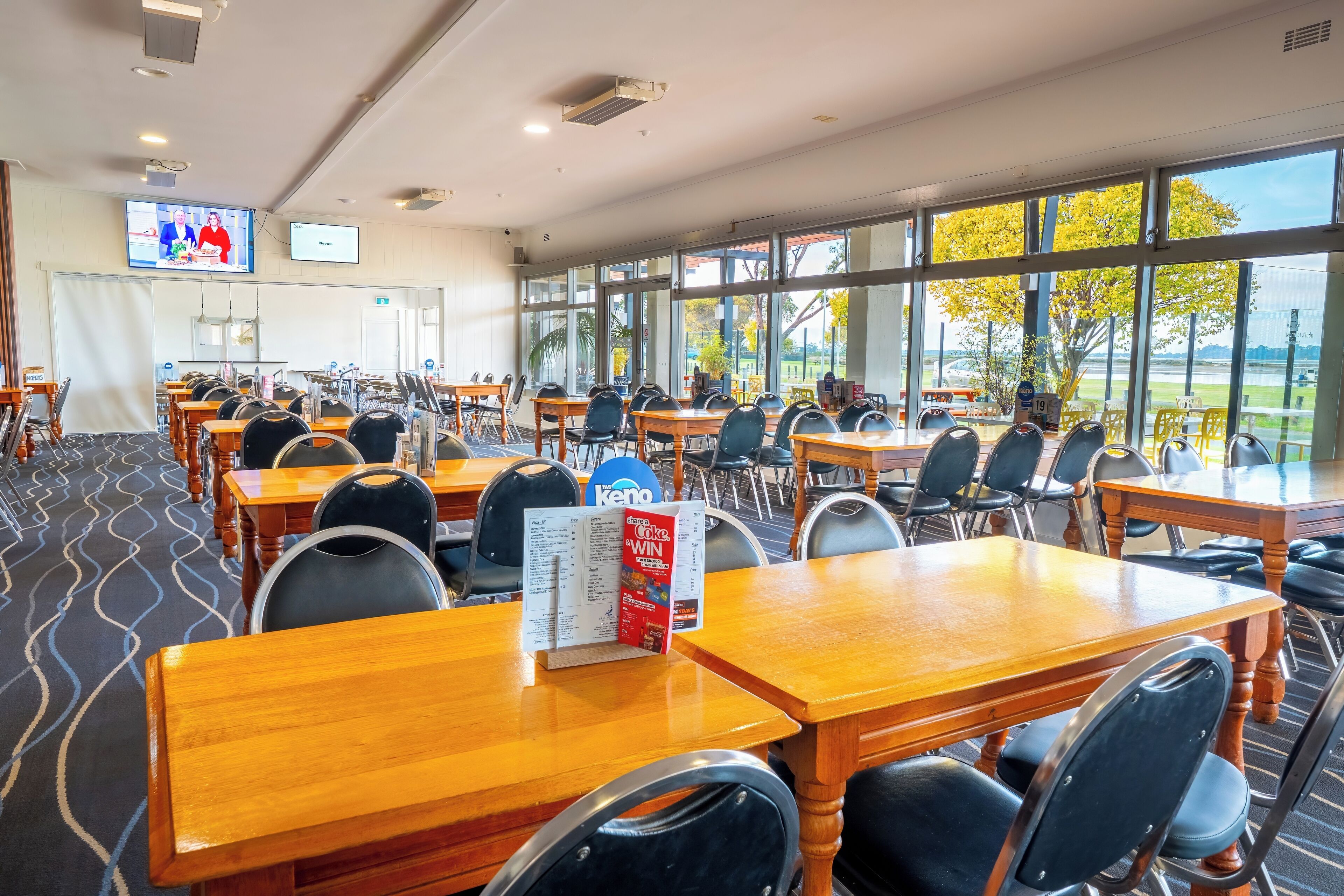 A conference room with tables and chairs, large windows, and a television screen.