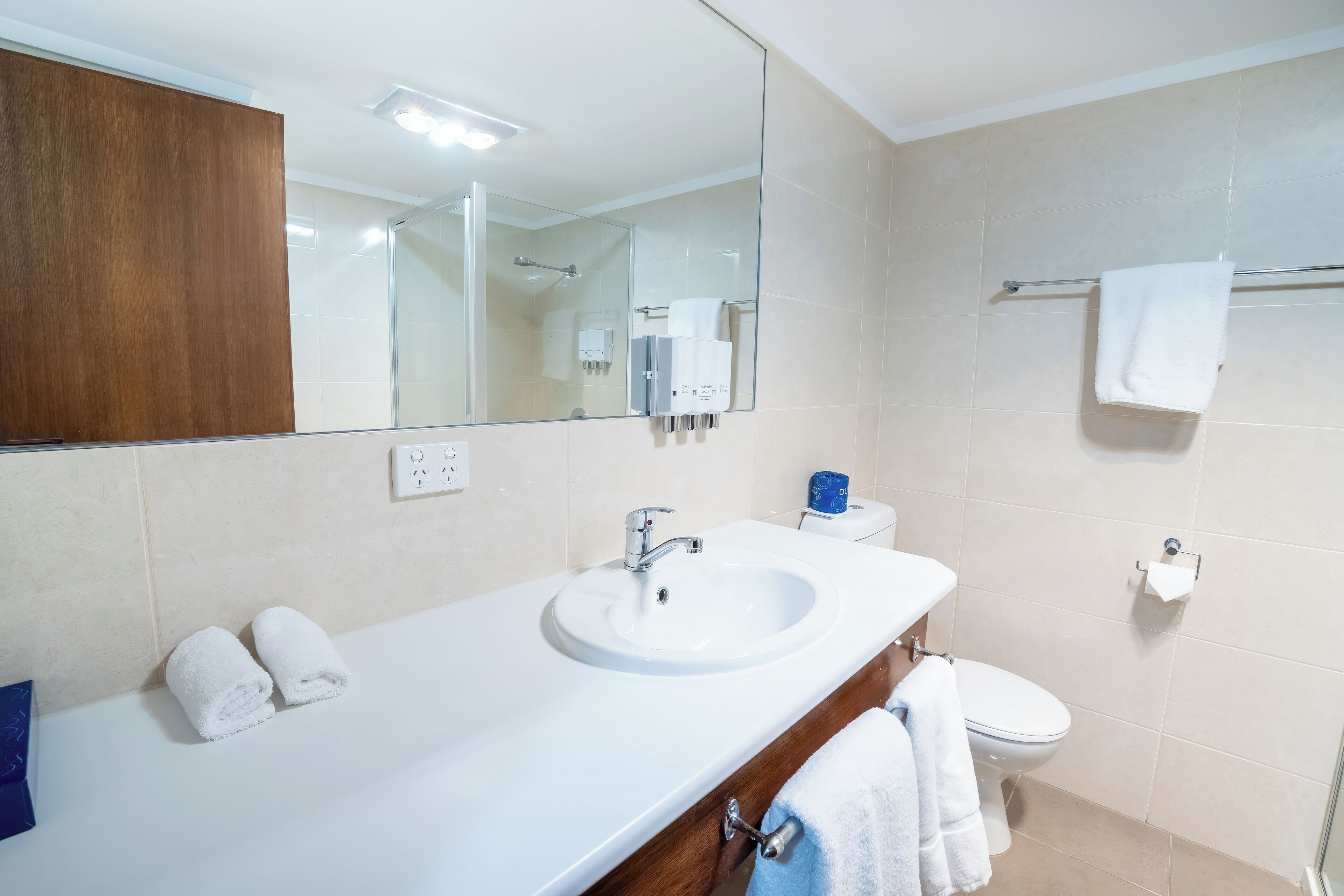 Un baño con lavamanos blanco, espejo, inodoro y toallero.