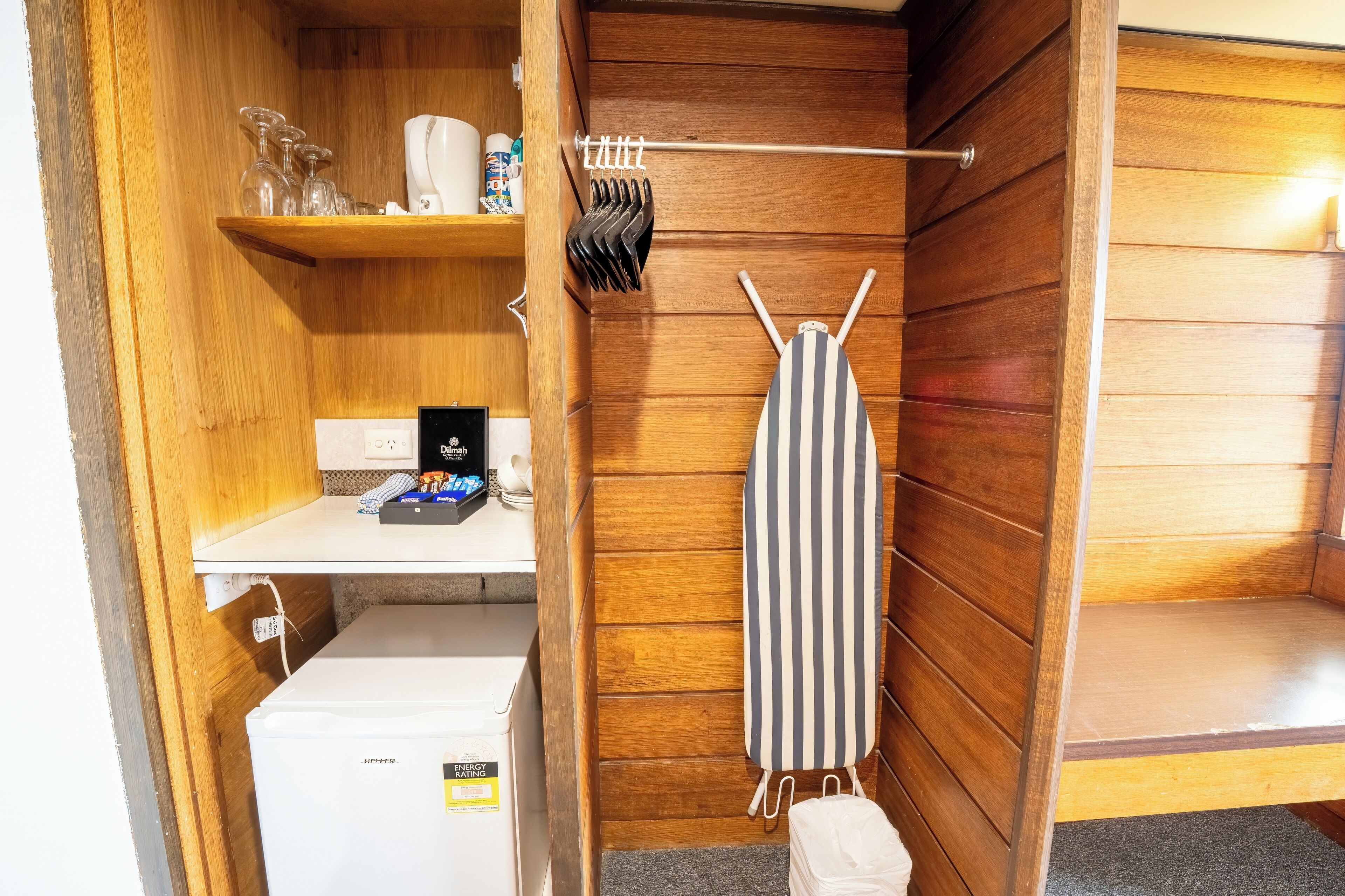 A compact room with a wooden interior, a small refrigerator, a shelf with toiletries, and a striped towel hanging.