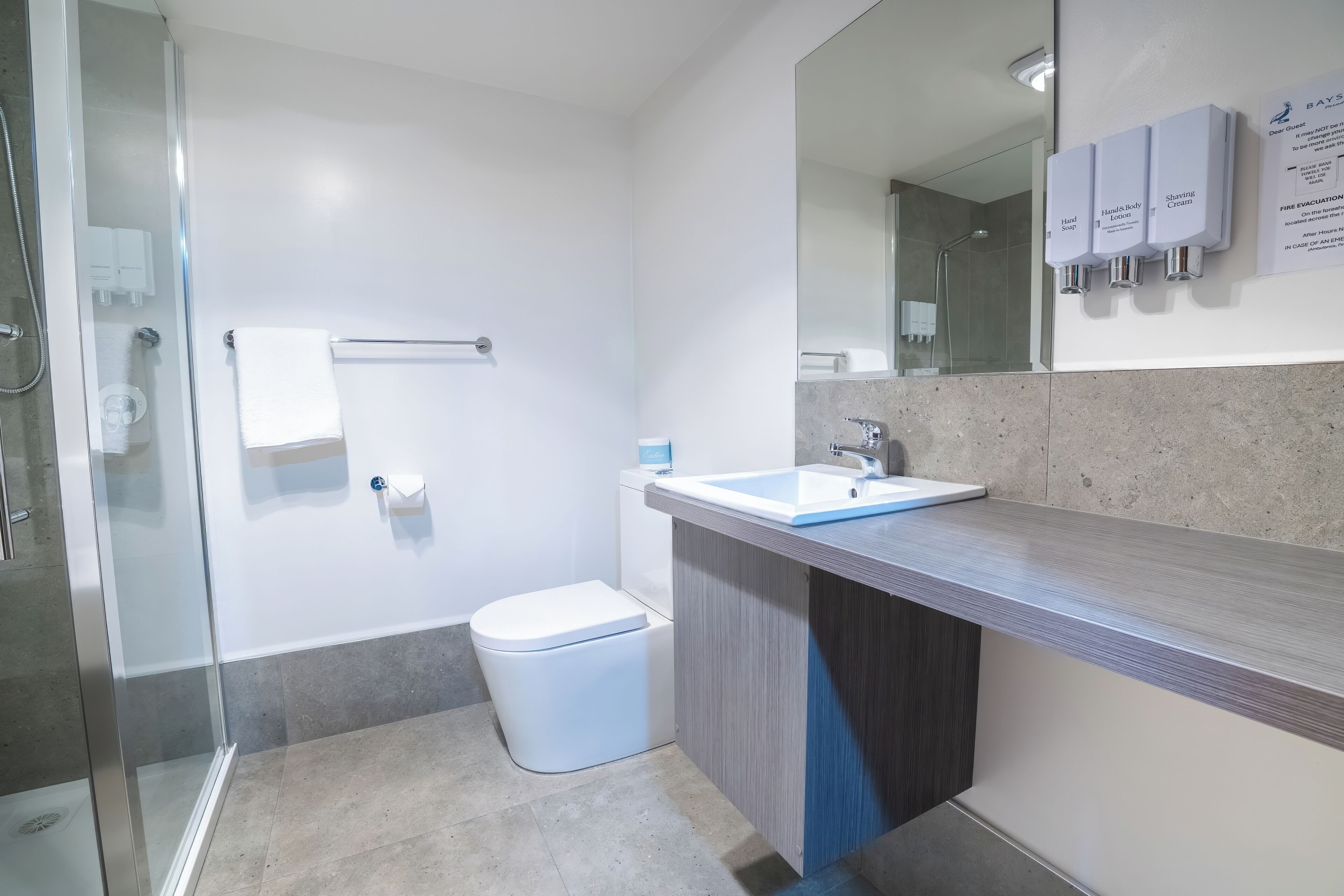 Une salle de bain moderne avec une douche à parois de verre, des toilettes blanches, un lavabo avec un miroir et un porte-serviettes.