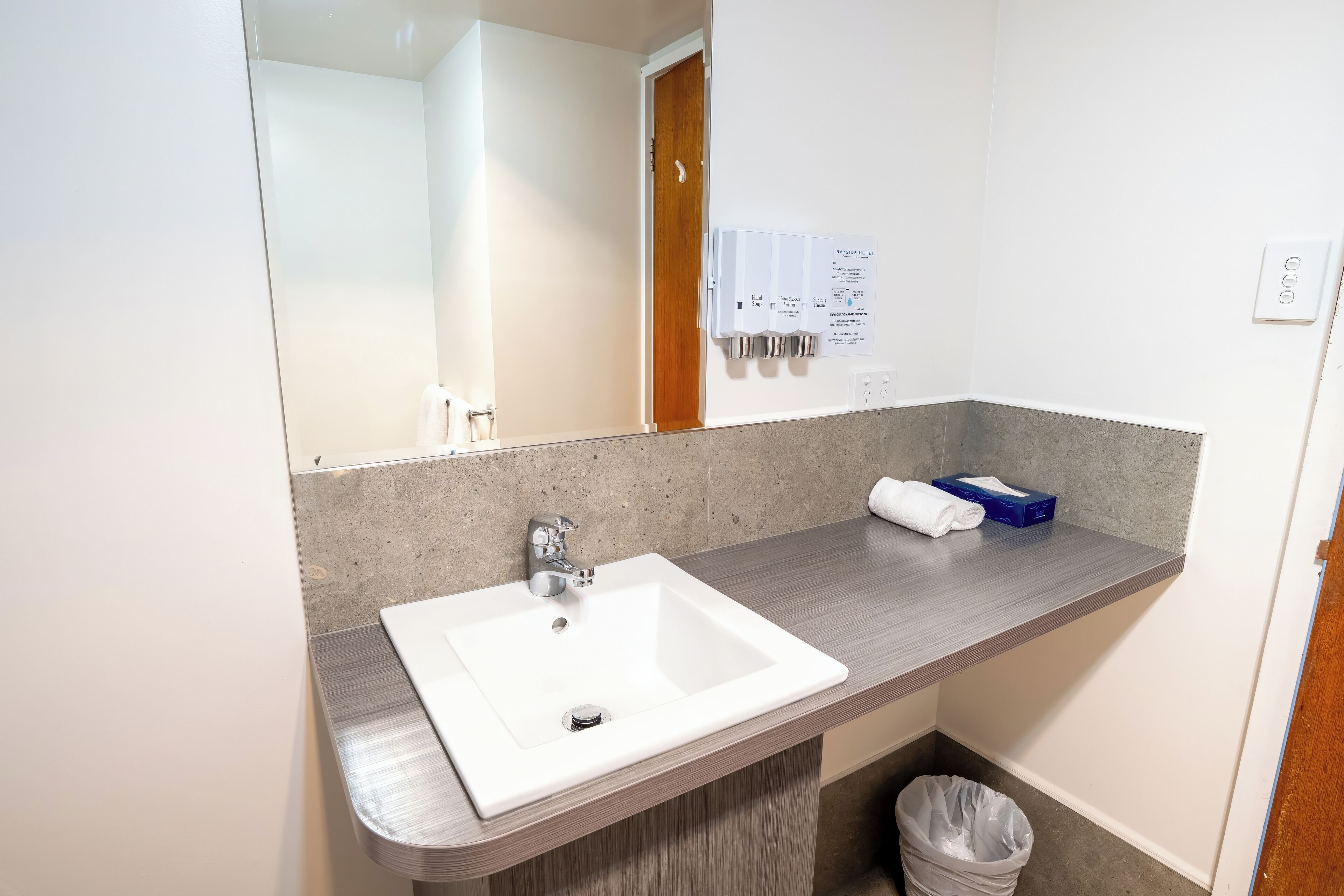 A hotel bathroom with a white sink, a mirror, a towel, and a hand soap dispenser.