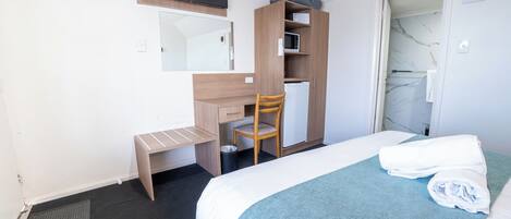 A hotel room with a bed, a desk, a chair, a wardrobe, and a bathroom visible through an open door.