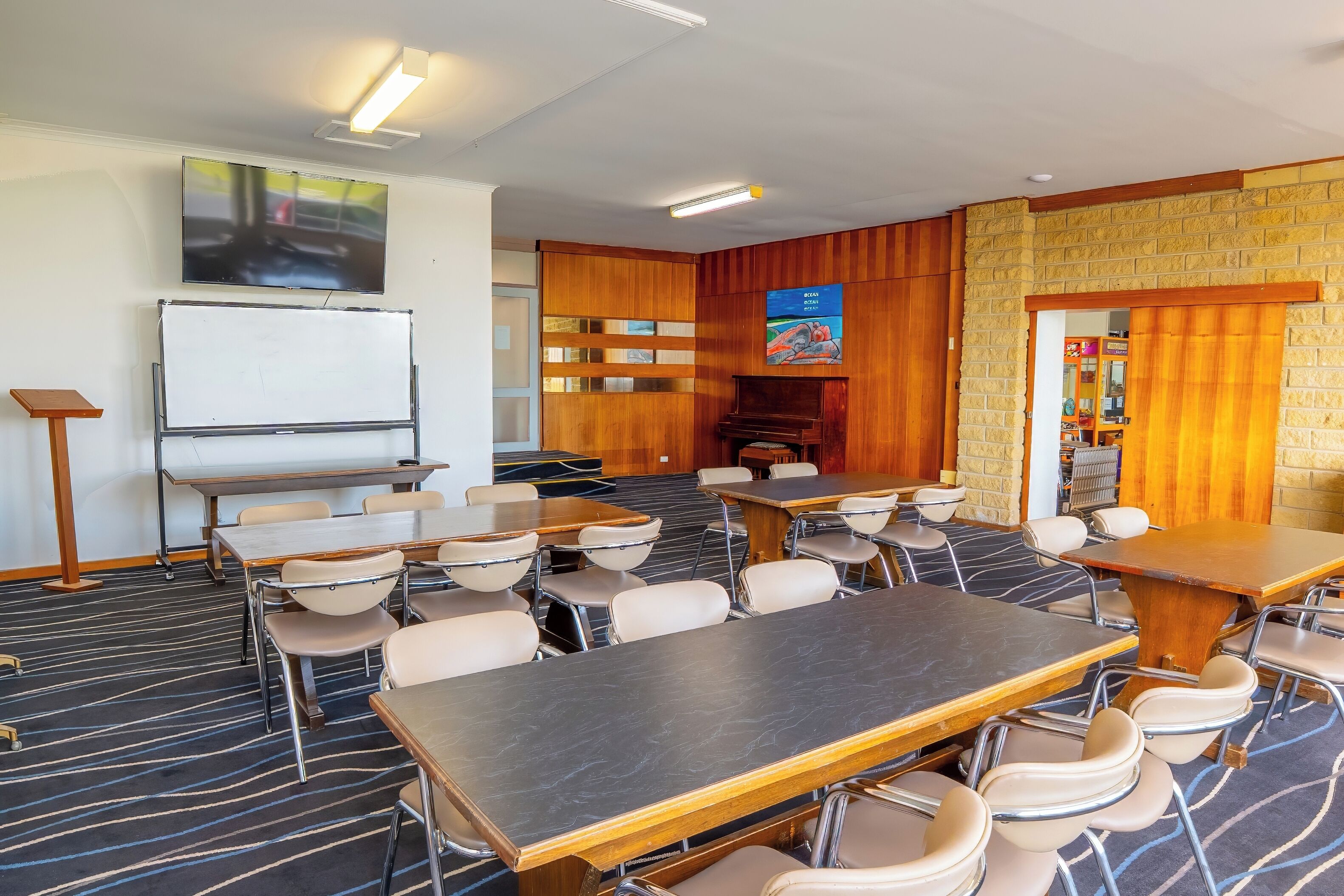 A conference room with tables and chairs, a whiteboard, and a piano.