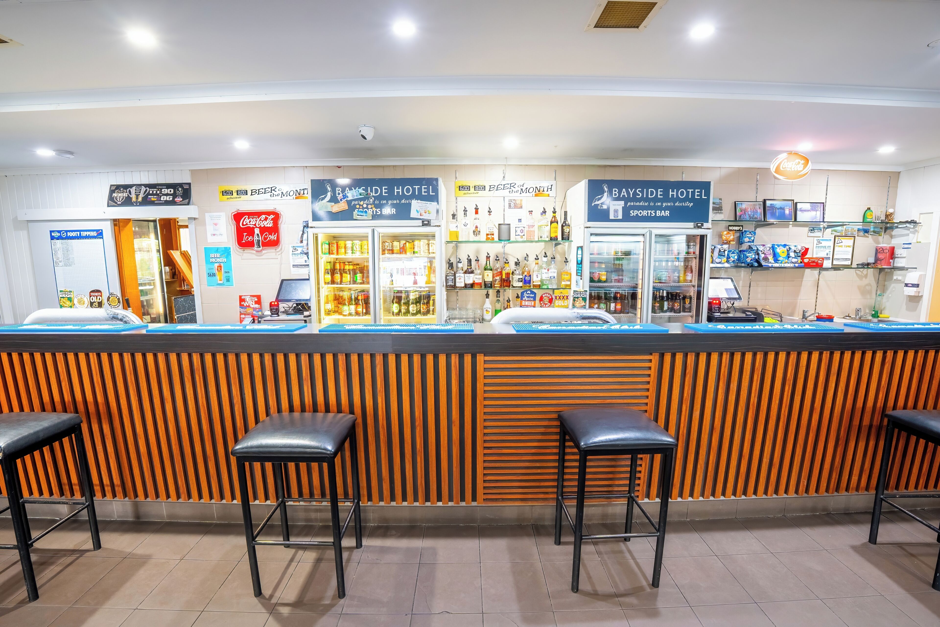 A hotel bar area with a counter, stools, and various signs indicating amenities like a sports bar and a Coca-Cola refrigerator.