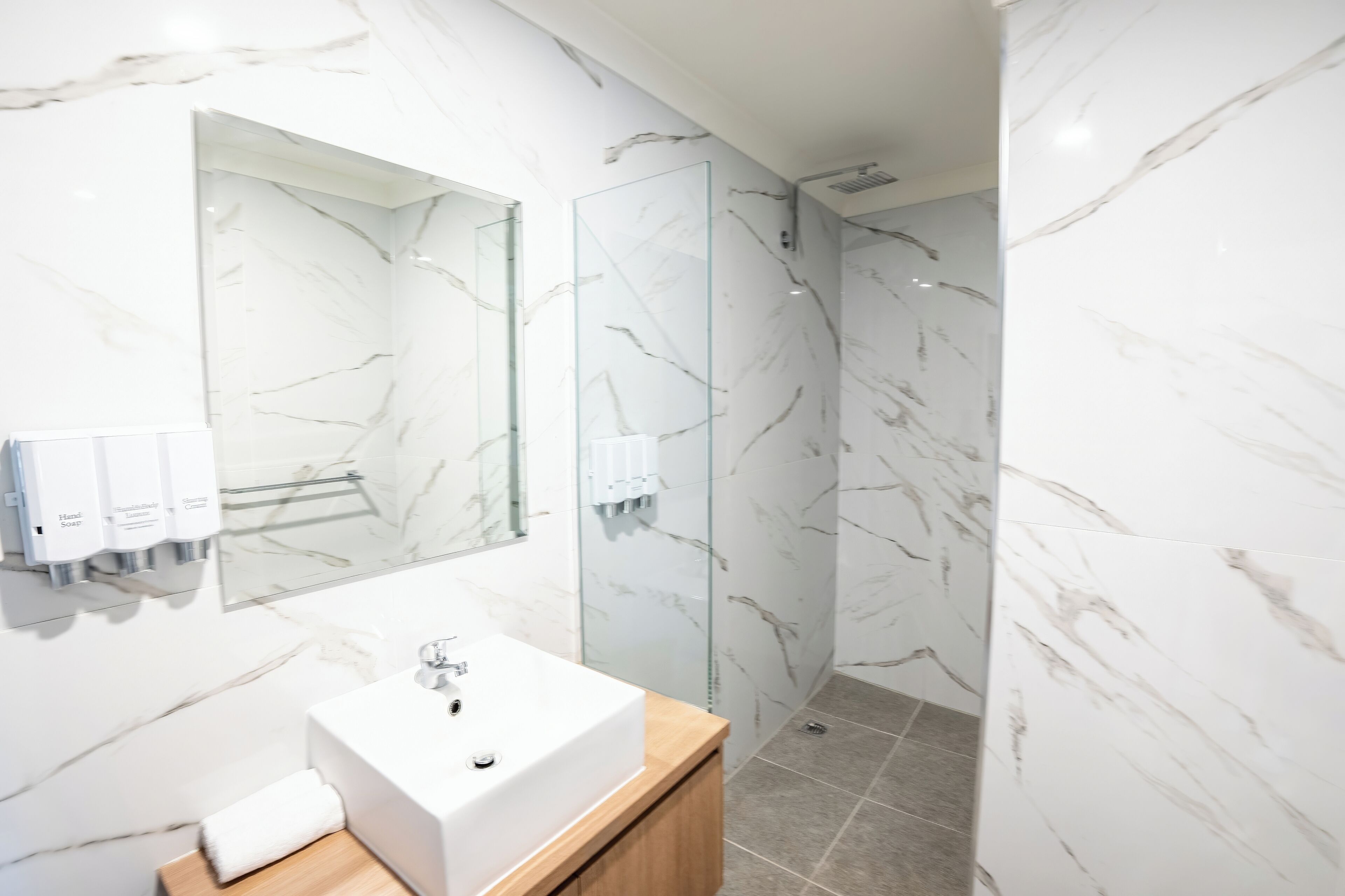 Un bagno moderno con una parete in marmo, uno specchio grande, un lavandino e un box doccia in vetro.
