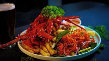 Une assiette garnie d’un homard, de frites et d’une salade, accompagnée d’un verre de bière.