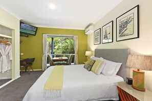 Habitación de hotel con una cama grande, un televisor montado en la pared, un balcón con vistas a la vegetación y un escritorio con una silla.