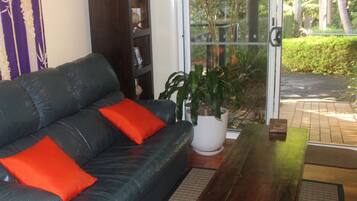 A living room with a black leather sofa, red cushions, a wooden coffee table, a white potted plant, and a bookshelf.
