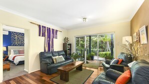 Ein Wohnzimmer mit einem dunkelbraunen Ledersofa, einem Holztisch und Blick ins Freie durch eine Glastür.