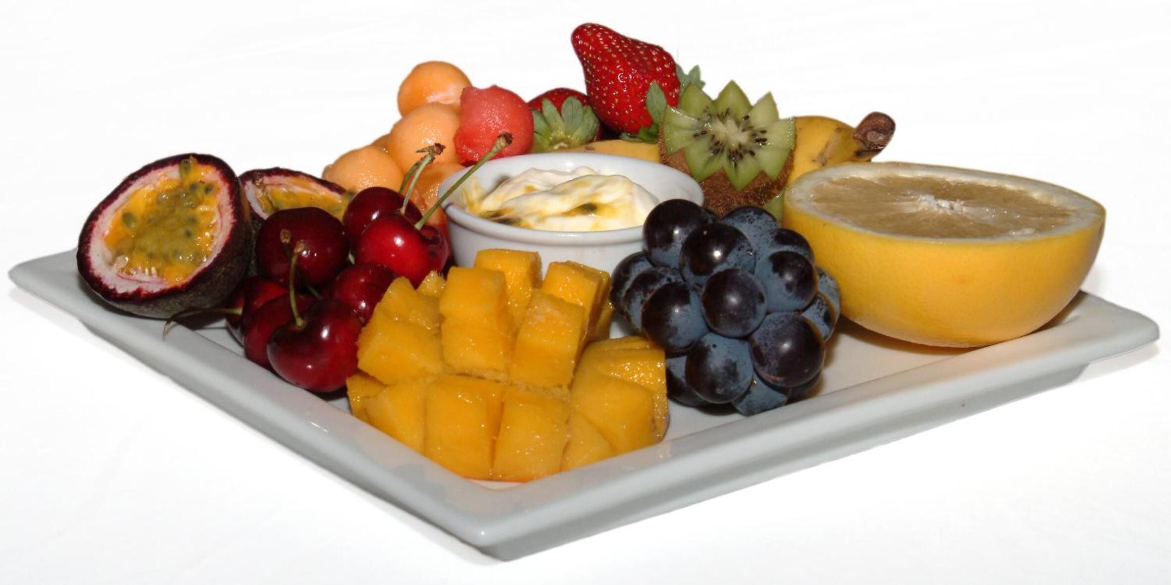 Verschillende soorten fruit, zoals mango’s, druiven, aardbeien en kiwi, op een wit bord.