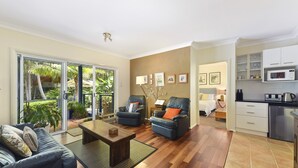Ein modernes Wohnzimmer mit einer Couch, Sesseln, einem Couchtisch und Blick auf einen Garten durch Glastüren.