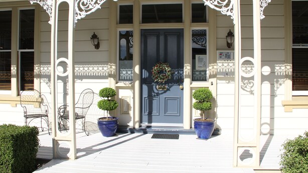 A building with a white facade, a dark blue door, and two potted topiary plants on the porch. - Merivale Manor (Christchurch)