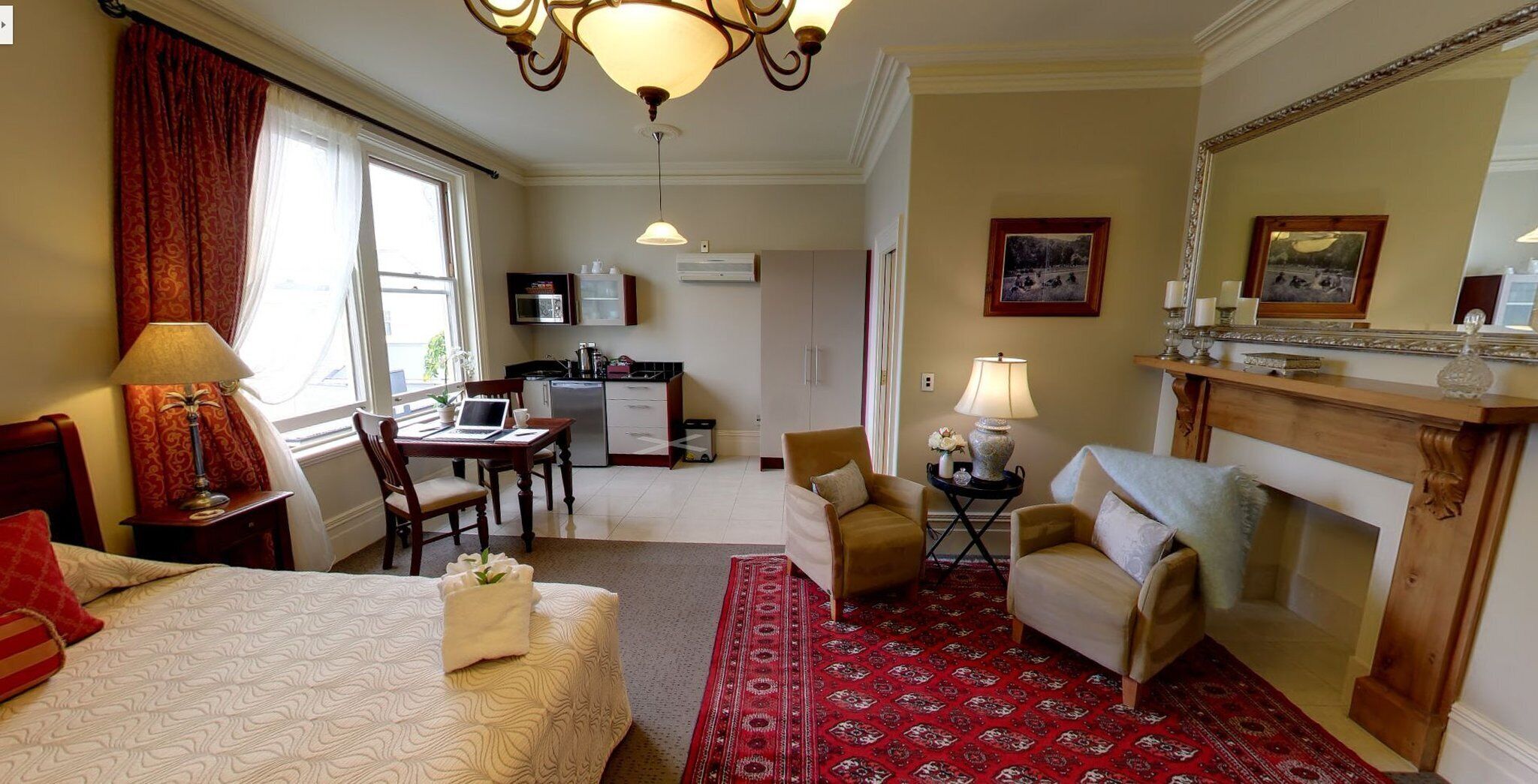 A hotel room with a bed, a desk with a laptop, a sofa, a fireplace, and a kitchen area.