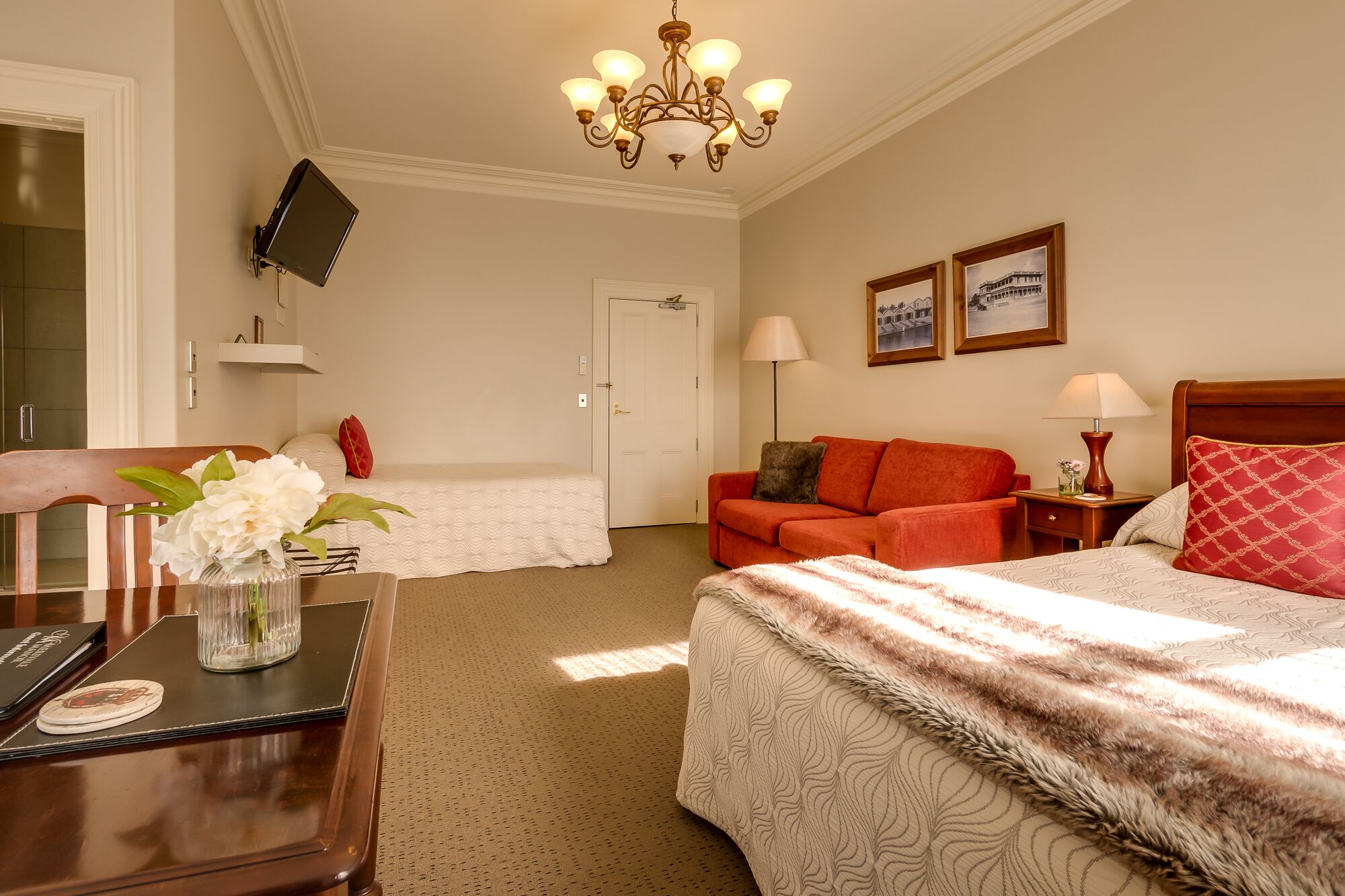 Ein Hotelzimmer mit einem Bett, einer Couch, einem Schreibtisch mit Lampe, einem an der Wand befestigten Fernseher und einer Deckenleuchte.