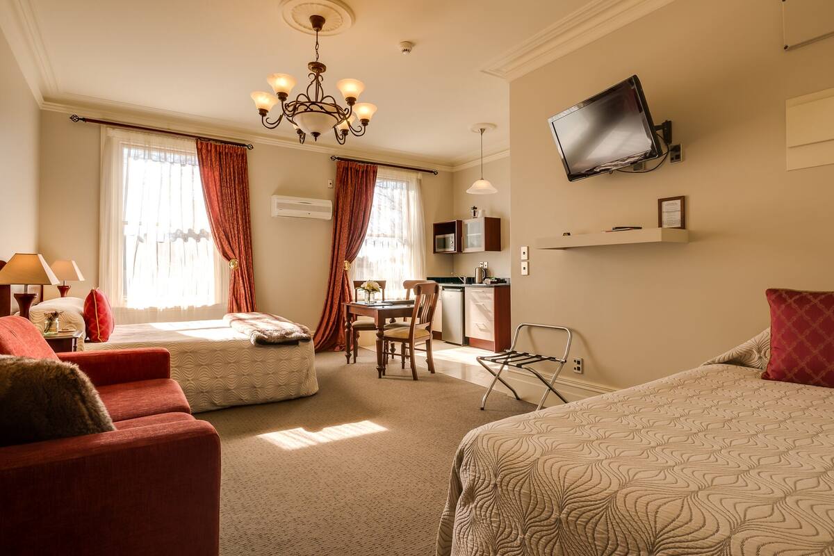 Une chambre d’hôtel avec deux lits, un coin repas, une cuisine et un téléviseur fixé au mur.
