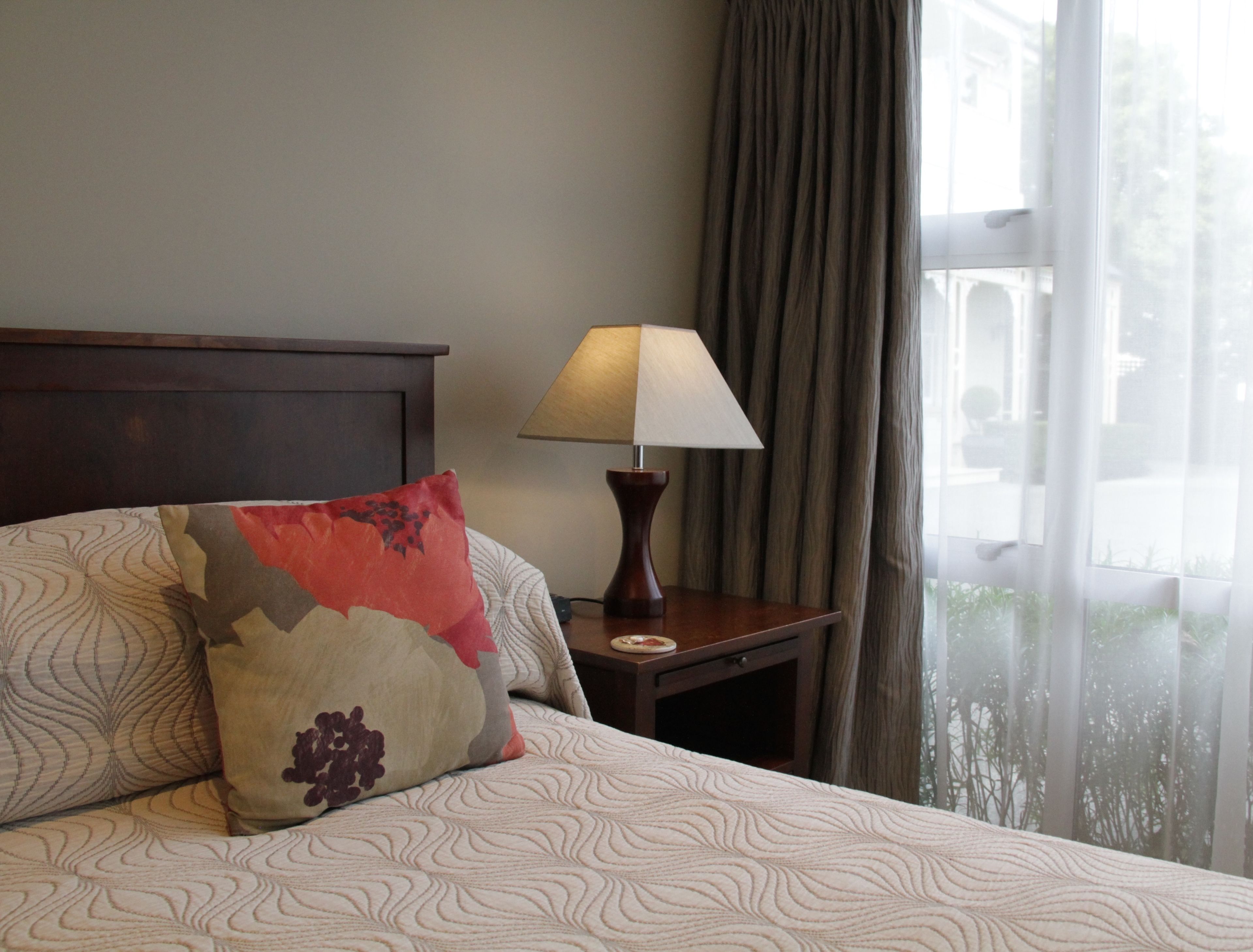 Una cama bien hecha con ropa de cama estampada, una lámpara de noche y una ventana con cortinas.