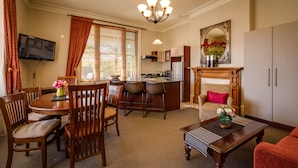 A dining area with a wooden table and chairs, a kitchen with a bar, and a living room with a sofa and a fireplace. - Merivale Manor (Christchurch)