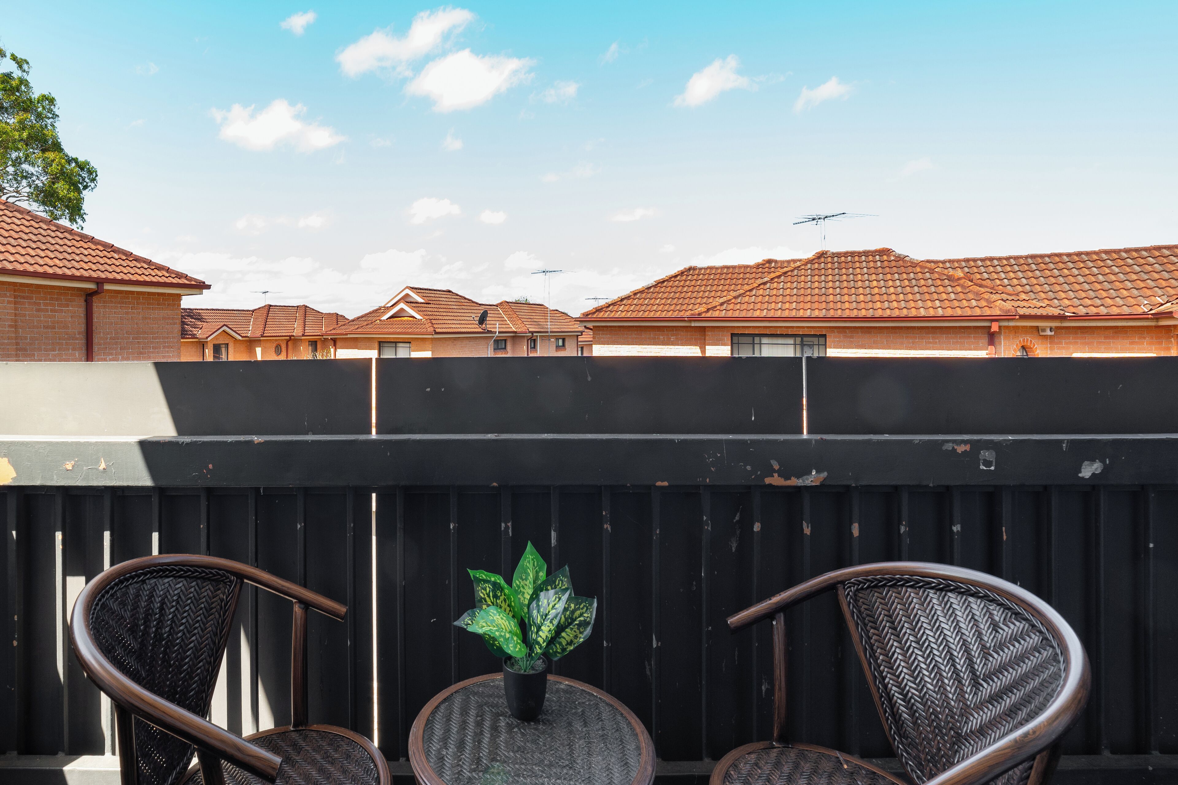 Una terraza en la azotea con dos sillas de mimbre, una planta en maceta y vistas a edificios residenciales.