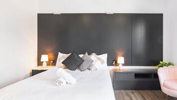 Et moderne hotelværelse med en stor seng, sengeborde med lamper, en mørk sengegavl og en lyserød stol.
