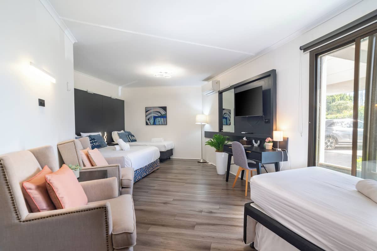 Una habitación de hotel con cama, dos sofás, escritorio, televisor y un ventanal grande.