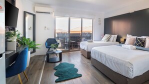 Habitación de hotel moderna con una cama grande, un escritorio, una silla y un balcón con vistas a edificios.