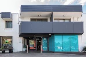 A modern building with a reception area, a vending machine, and a large glass window reflecting the surroundings. - Bankstown Motel 10 (Greenacre)