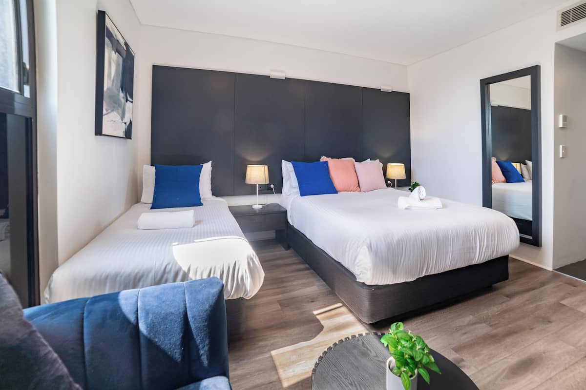 Una habitación de hotel moderna con dos camas, un sofá, una mesita y un espejo.