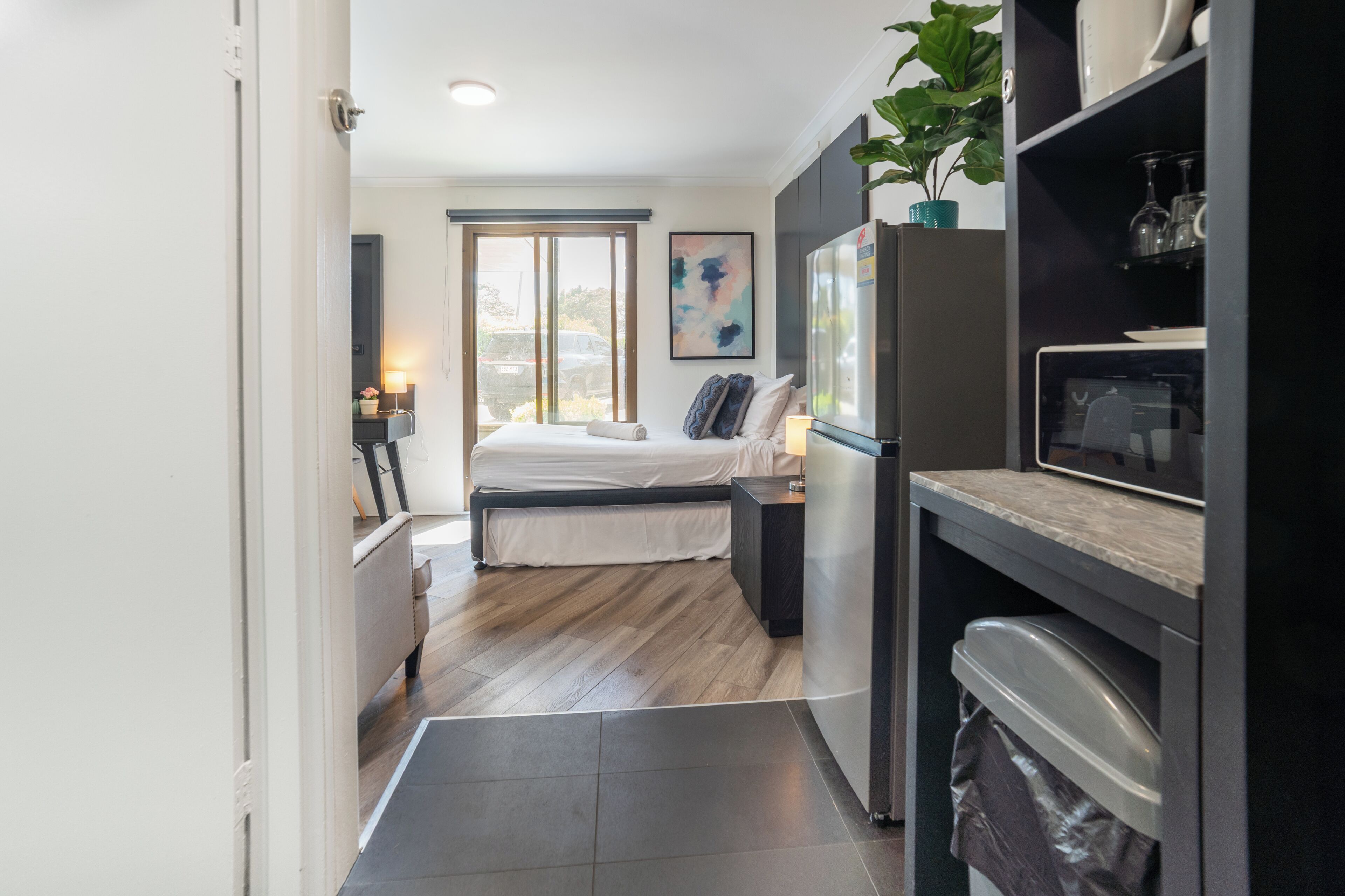 Una habitación compacta con cama, kitchenette y un ventanal amplio.