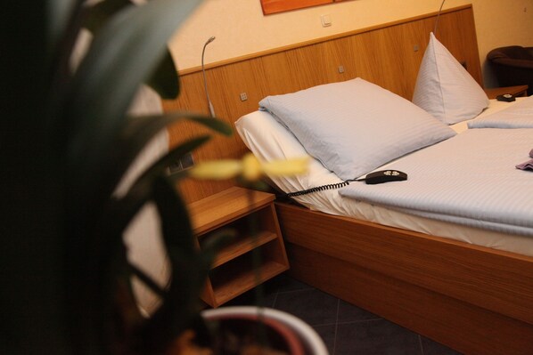 A neatly made bed with a wooden headboard, a bedside table, and a potted plant.