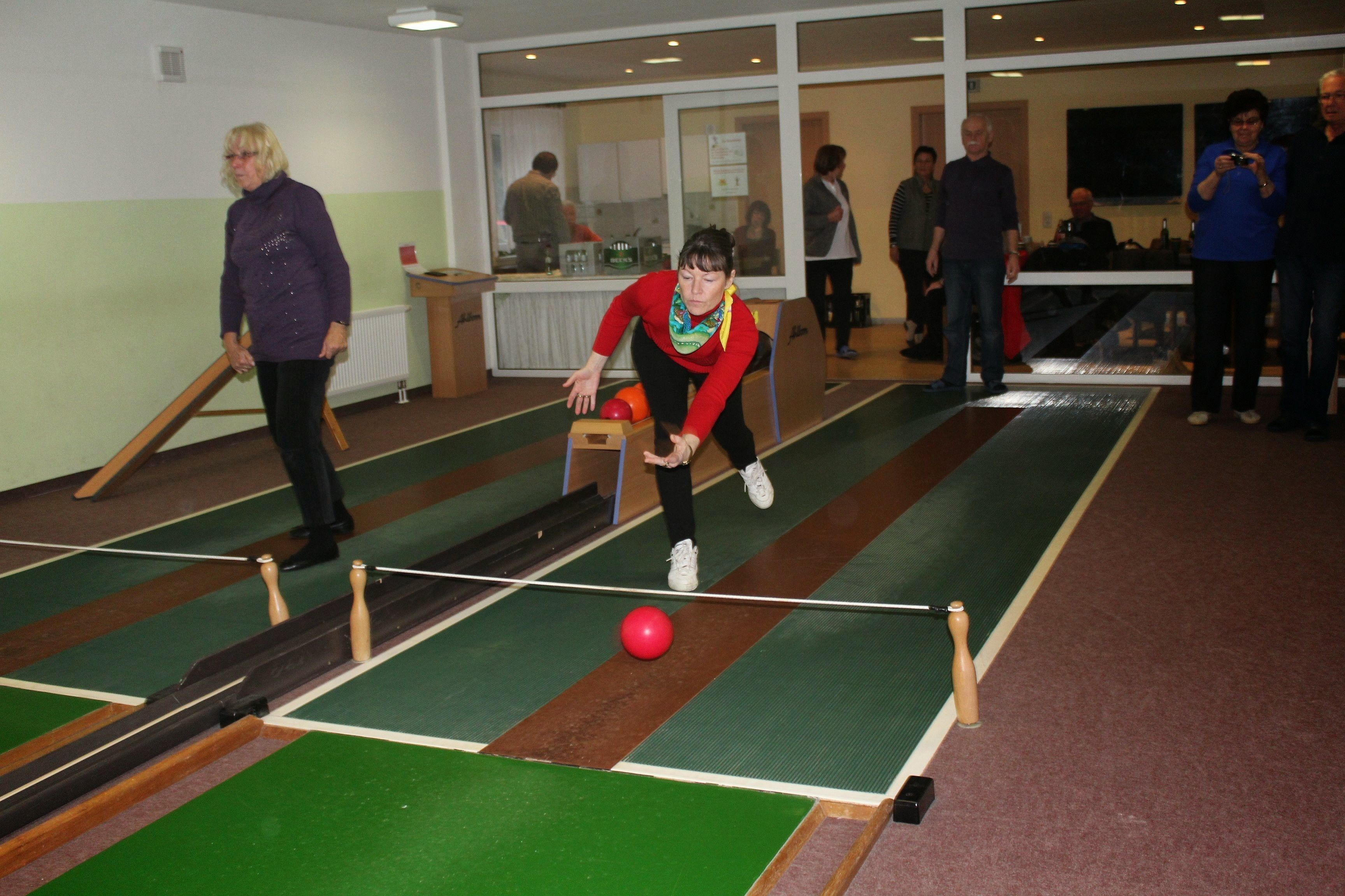 A bowling alley with multiple lanes, a red bowling ball, and people playing.