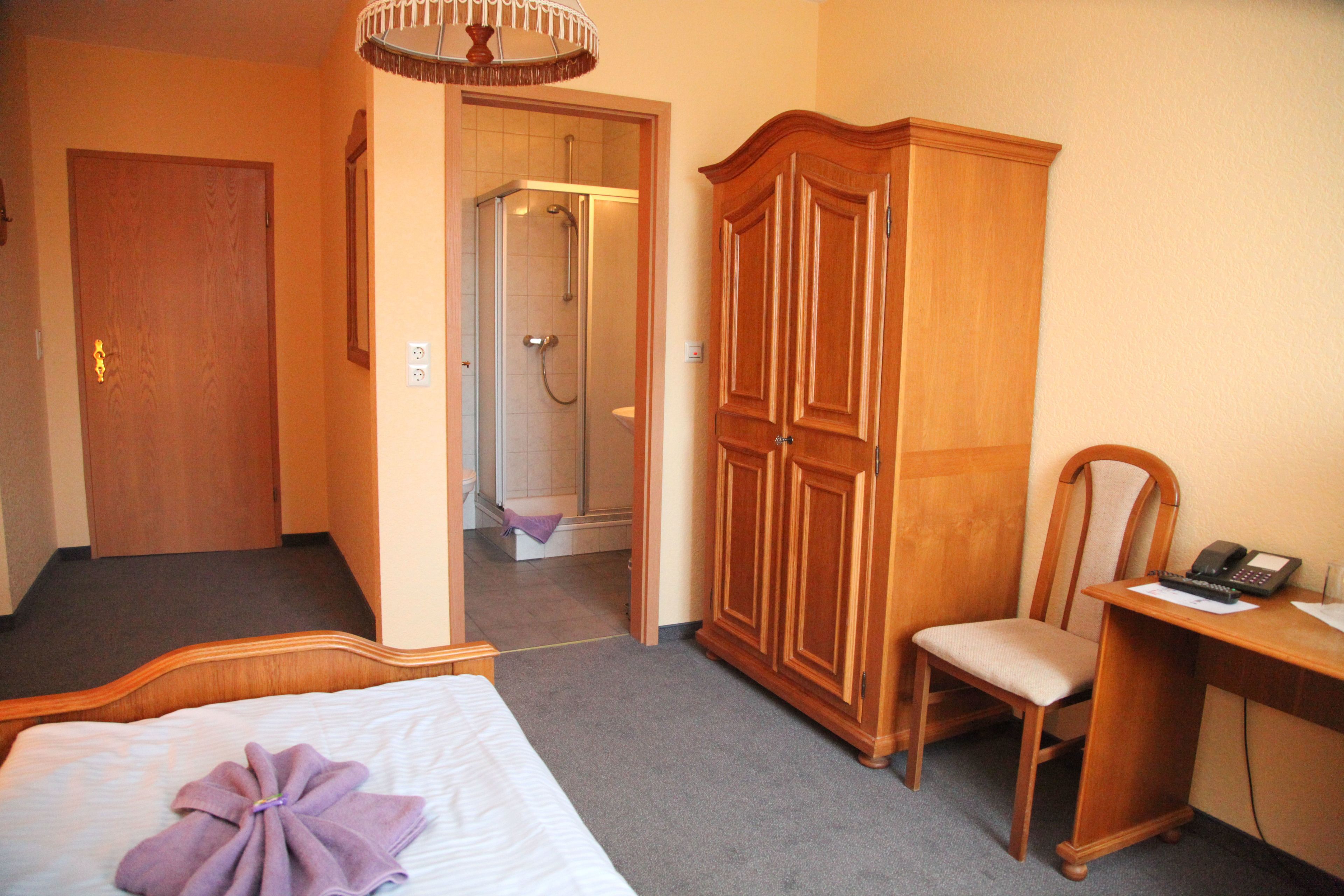 Habitación de hotel con cama, armario de madera, escritorio con silla y zona de ducha.