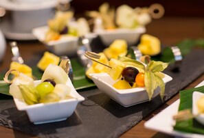 A series of small white dishes containing fruit and a decorative key, arranged on a black slate serving board.