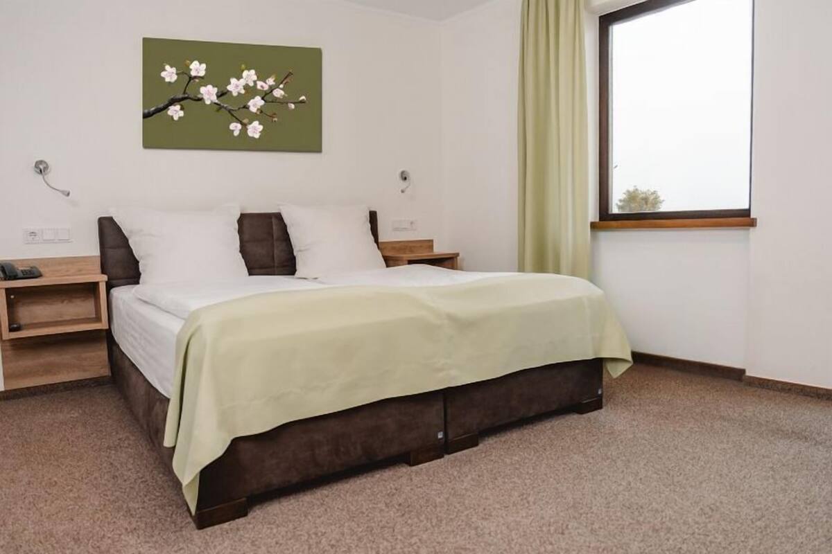 Een keurig opgemaakt slaapkamer met een bed, nachtkastjes en een raam met gordijnen.