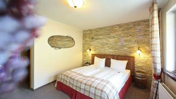 A bedroom with a stone wall, a wooden headboard, a bed with a plaid bedspread, two bedside lamps, a telephone, and a wooden barrel.