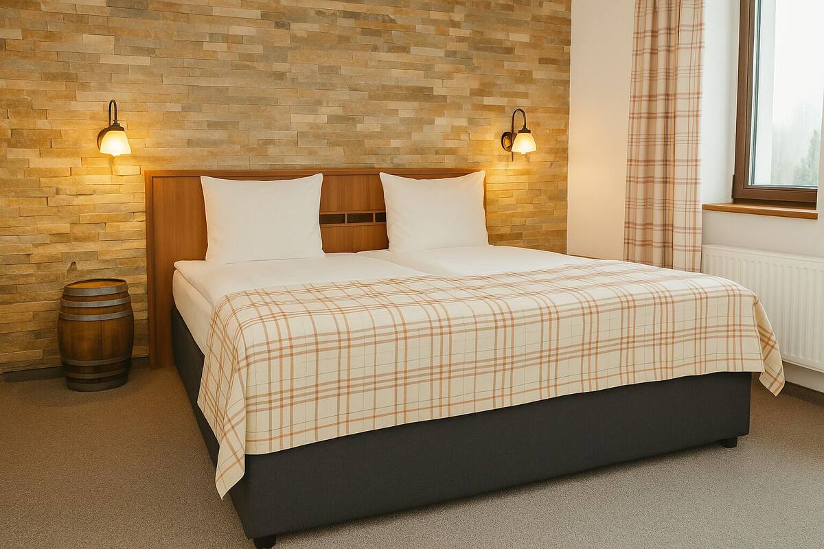 Een slaapkamer met een houten hoofdeinde, twee bedlampen, een geruite sprei, een houten vat en een raam met gordijnen.