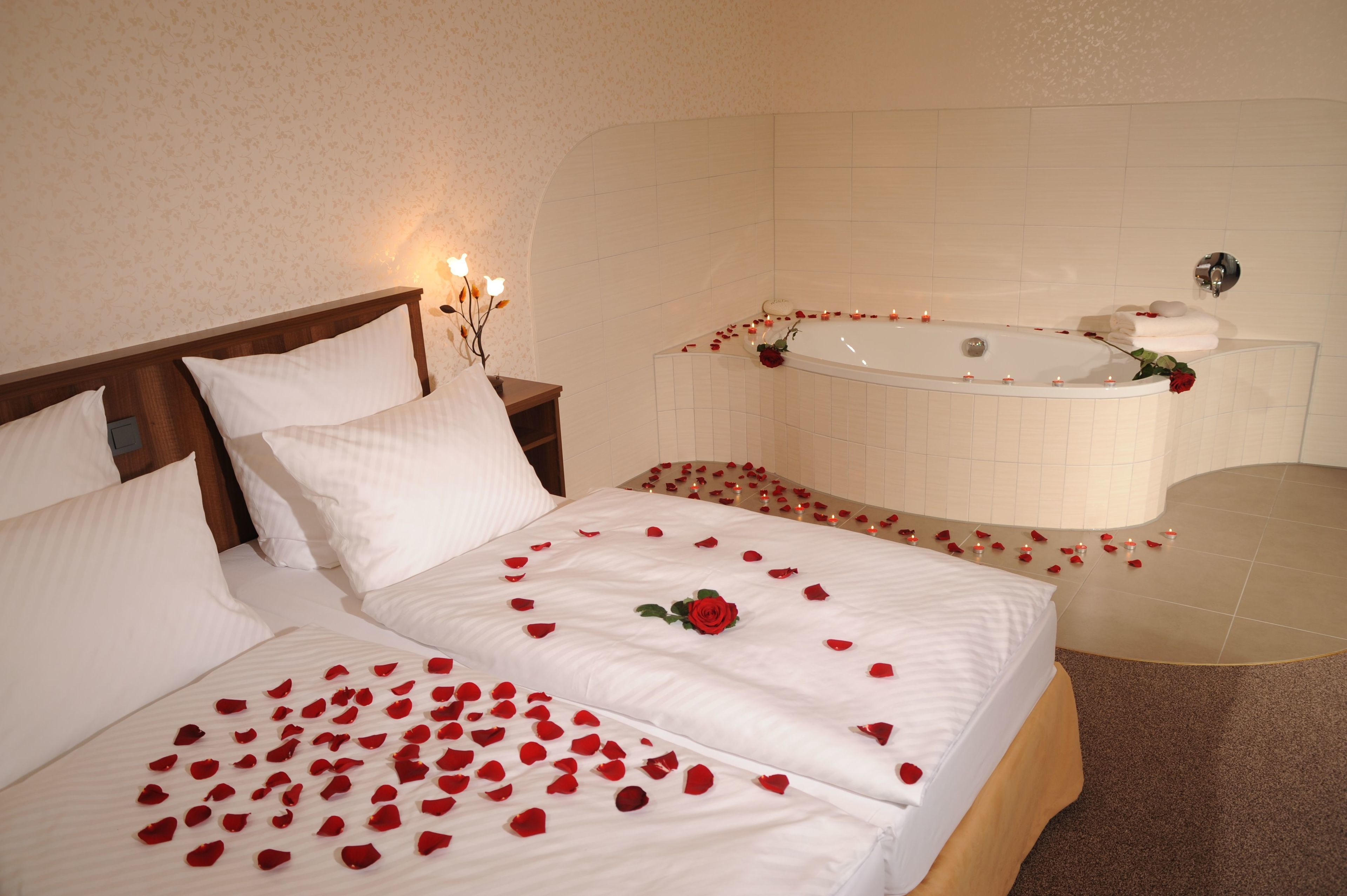 Een hotelkamer met een groot bed, een vrijstaand bad en een klein tafeltje met kaarsen.