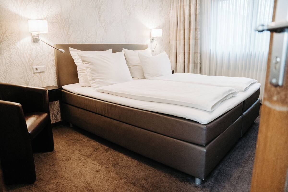 Een keurig opgemaakt bed met witte lakens, een hoofdbord en twee bedlampjes.