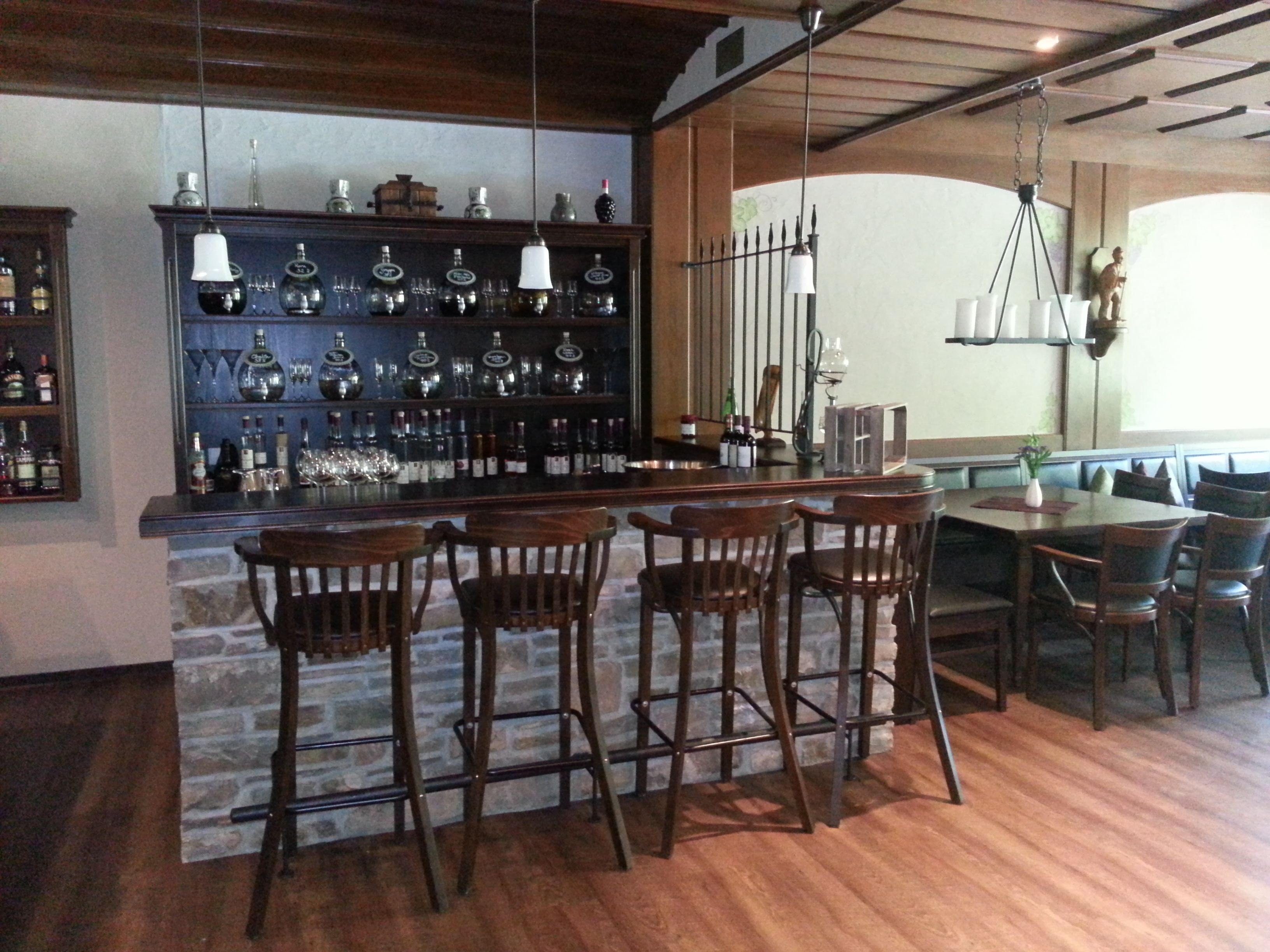 Eine Bar mit Holzhockern, einer Steinwand und Regalen mit Flaschen und Gläsern.
