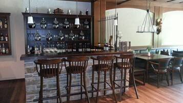 A bar area with wooden stools, a stone wall, and shelves with bottles and glasses.