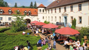 An outdoor seating area with red umbrellas and tables, surrounded by buildings with traditional architecture. - Fröbelhof (Bad Liebenstein)