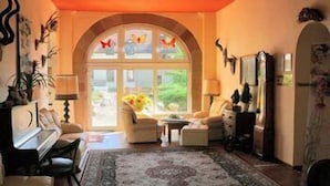 A cozy living room with a large arched window, a piano, and a fireplace. - Fröbelhof (Bad Liebenstein)