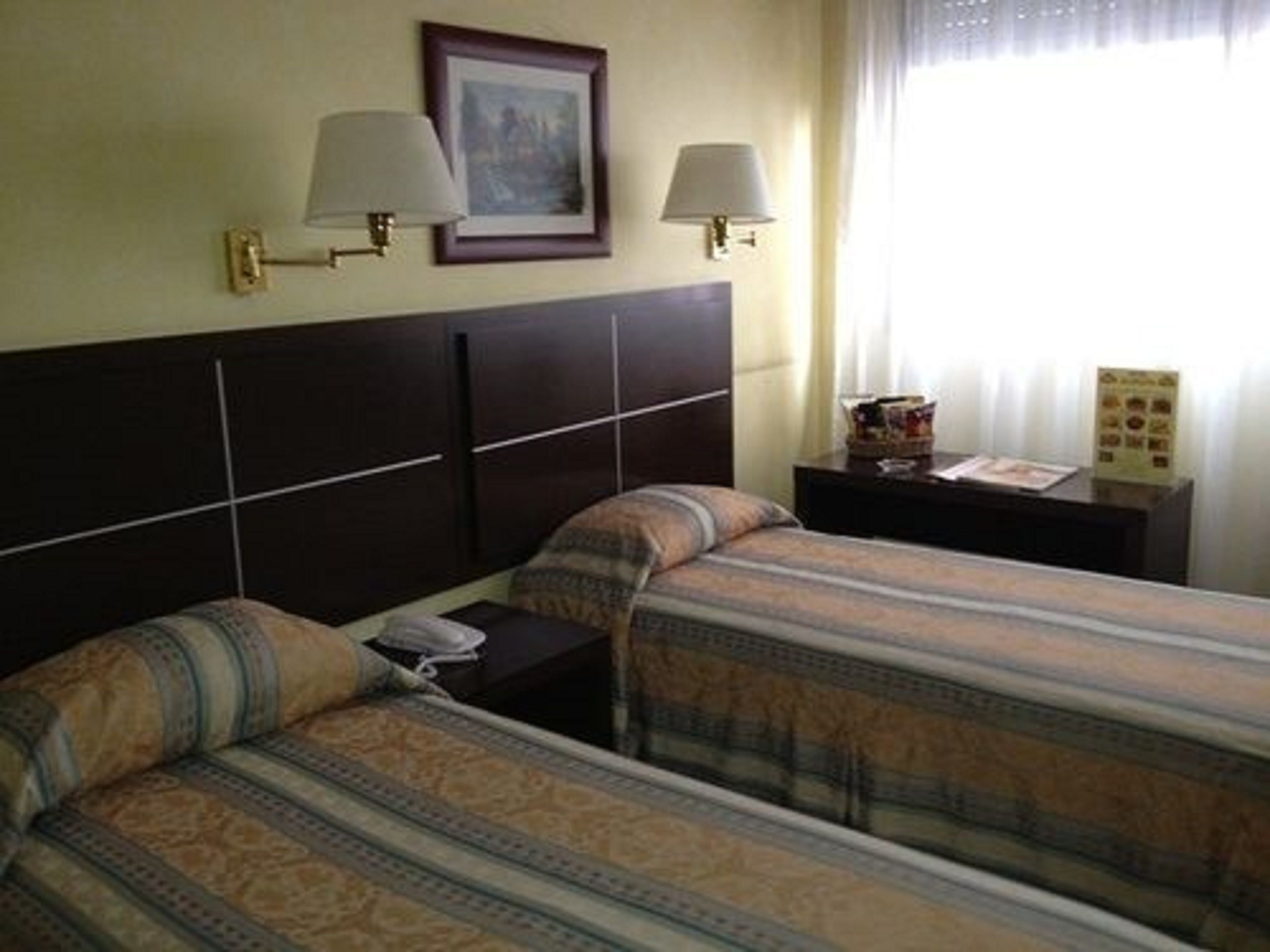 Una habitación de hotel con dos camas, cada una con una colcha estampada, una mesita de noche con lámpara y un cuadro enmarcado en la pared.