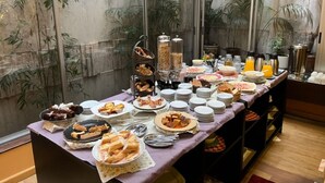 Montaje tipo bufé con diferentes opciones de comida y bebidas, incluyendo una cesta de pan, un bol de frutas y una estación de café.