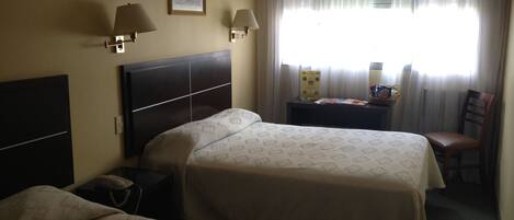 Una habitación de hotel con dos camas, un escritorio, una silla, un televisor y una ventana con cortinas.