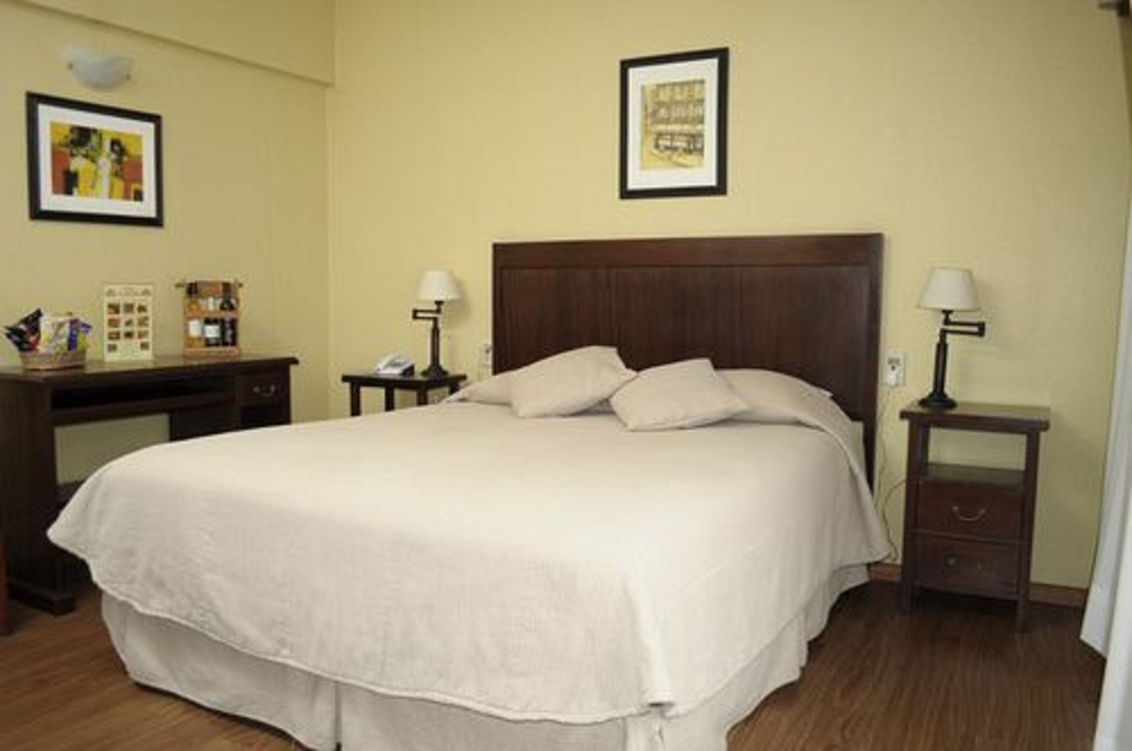 A neatly made bed with a wooden headboard, a bedside table with a lamp, and a small nightstand with a lamp.